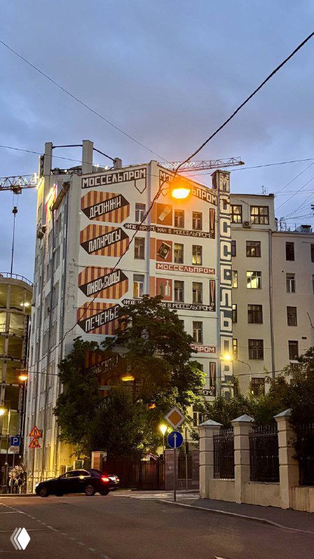 Большая настенная роспись и архитектурные фасады на фоне вечернего неба — городской пейзаж в районе Большого Кисловского переулка.