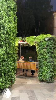 Деревянная скамейка-качели, обвитая зеленью и растениями, на тихой аллее — финал прогулки после ужина в Layerz.