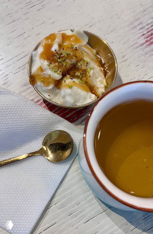 Малаби в прозрачной пиале с фисташками и соусом из инжира, рядом чайник и чашка с настоем — нежная текстура десерта на столе.