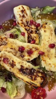 Крупный план жареного халуми на листьях салата с зернами граната и дольками томата на пастельно-розовой тарелке