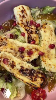 Деталь салата с жареным халуми: полоски сыра с поджаренной корочкой, гранатовые зёрна, томаты черри и хрустящие листья салата.