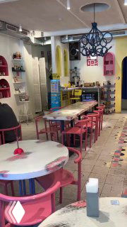 Интерьер кафе Абу Гош: розовые и пастельные столы, стулья и декоративные элементы, светильник и открытое пространство для гостей.