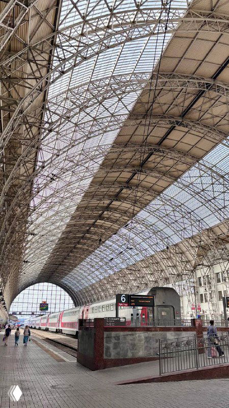 Арочная стальная кровля дебаркадера над путями Киевского вокзала: длинная перспектива платформы, вагон на путях и железная конструкция крыши.