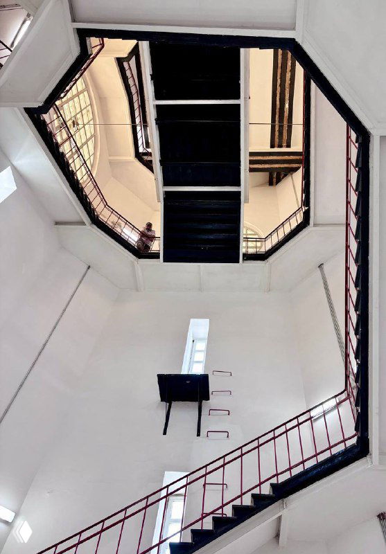 Вид внутрь восьмиугольной лестничной шахты второго этажа вокзала: перила, ступени и вертикальная перспектива на потолочные окна сверху.