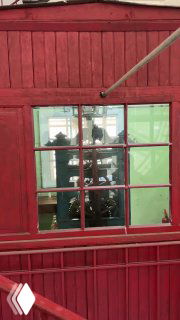 Красная будка часовщика с видимым через окно механизмом больших башенных часов; интерьер служебного помещения внутри часовой башни вокзала.