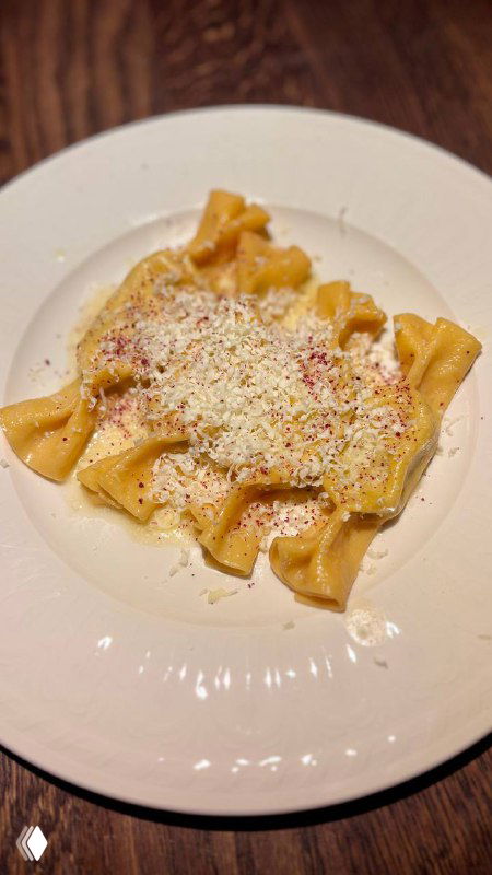 Крупный план тарелки пасты с рикоттой и кейлом на деревянном столе; видна кремовая текстура, тёртый сыр и тёплая сервировка блюда