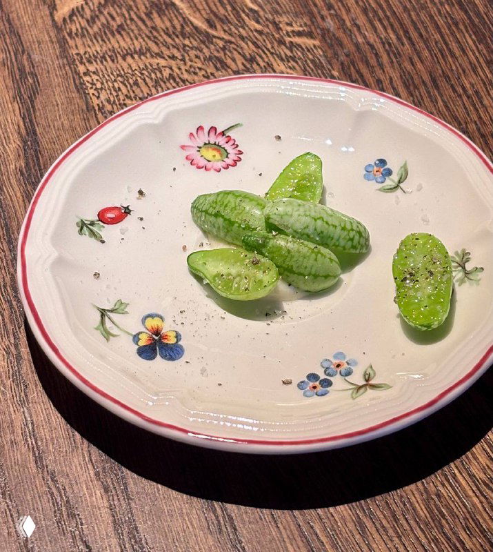 Мелотрия — мини-огурцы в необычной раскраске, сервированные в простой белой тарелке на деревянном столе — акцент на фермерских продуктах