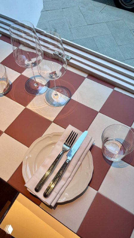 Сервировка на столе у окна: стеклянная посуда, приборы и клетчатая скатерть; дневной свет создаёт уютную атмосферу ресторана