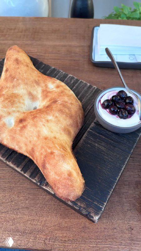 Лодочка шоти, крупный хлеб из тандыра на деревянной доске рядом с небольшой миской варенья — подача из пекарни Bagebi под стеклянной крышей.