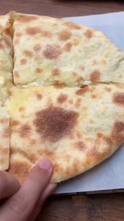 Разрезанный лепешковый хлеб (похоже на шоти) на подложке, видно текстуру мякоти и корочки, рука держит край хлеба крупным планом.