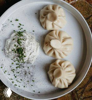 Тарелка с аккуратно сложенными хинкали и порцией кремового соуса — классическая подача пельменей по-грузински в Bagebi.