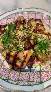 Кусочки жареного блюда с зелёным луком и соусом, поданные на узорной тарелке — крупный план сервировки в ресторане.