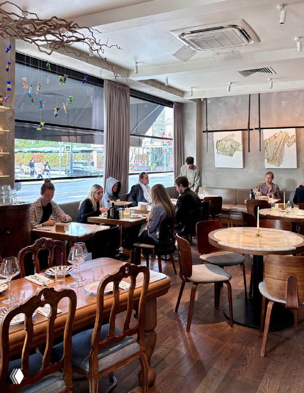 Интерьер Linbistro: зал с деревянными столами и стульями, большими окнами и естественным светом, вид на посетителей.