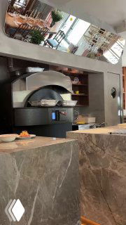 Фрагмент открытой кухни: дровяная или пекарская печь в зоне приготовления пиццы и рабочая поверхность ресторана.