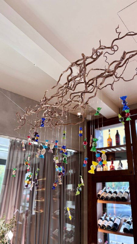 Декоративные подвесные украшения и полки с бутылками в интерьере ресторана — художественная инсталляция у окна.