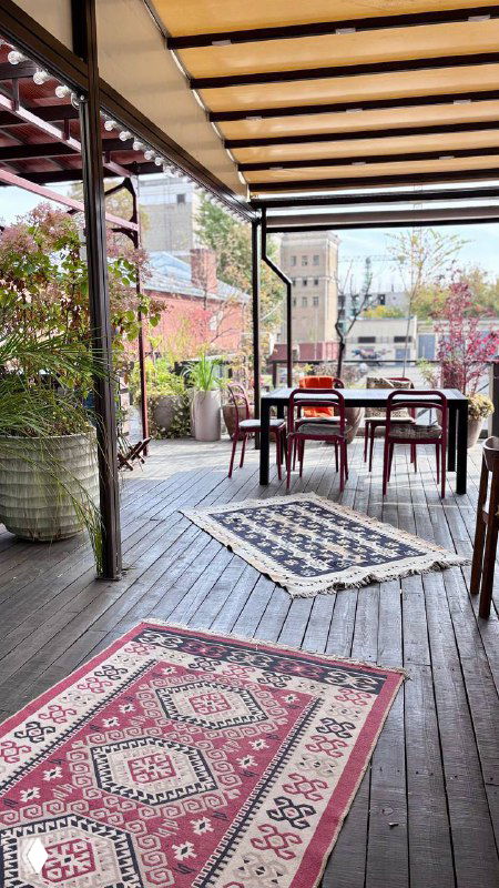 Открытая веранда ресторана Kilim в Красном Октябре: коврики, столы и деревянная пергола, вид на набережную и городской пейзаж в Москве.