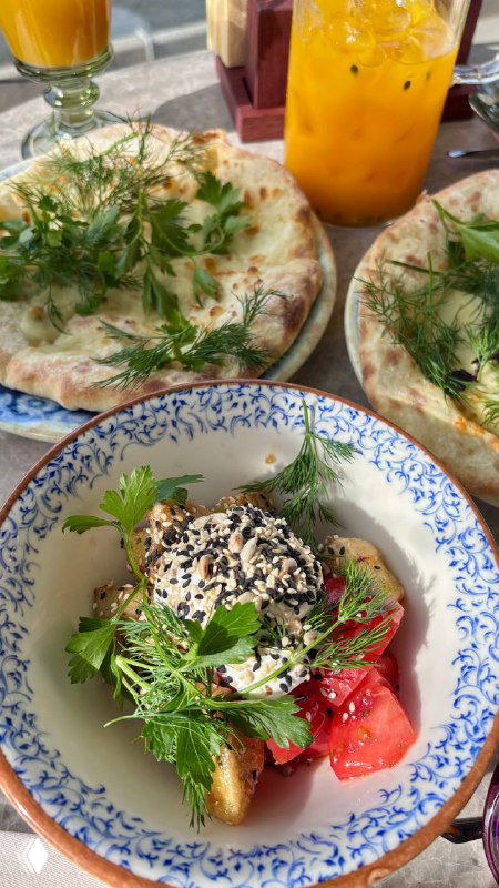 Тарелка с закуской и стакан домашнего лимонада: свежая зелень, сыр и помидоры на узорчатой керамике, близкий план в ресторане Kilim.