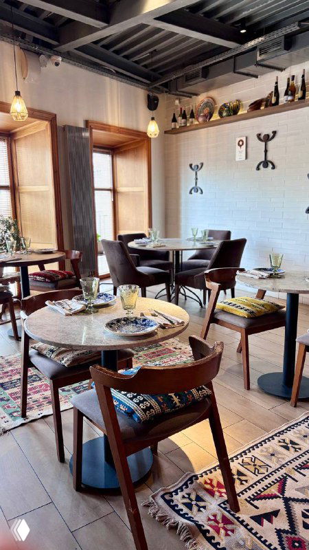 Уютный зал ресторана Kilim: столы, ковры на полу и деревянная отделка, мягкое освещение и композиция мебели для завтрака в Москве.