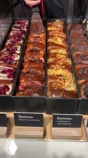 Крупный план бриошей в витрине: корочка, яркие начинки и текстура булочек, видно оформление и часть табличек с названиями.