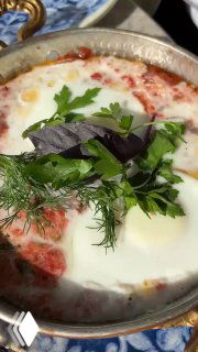 Блюдо с яйцом в томатном соусе, запечённое в небольшой сковороде и украшенное зеленью и базиликом, подано на столе Kilim в Москве.