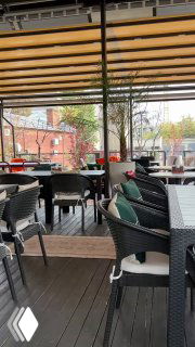 Веранда Kilim: столы и стулья под деревянной перголой, городская улица и краснокирпичные здания на заднем плане, ощущение летнего завтрака в Москве.