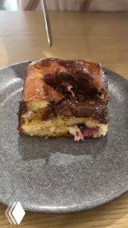 Кусочек бриоши на тарелке: видна слоистая текстура, заварной крем и кусочки вишни внутри, сервировка на столе.