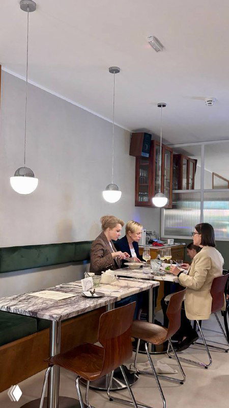 Гости за столом в зале Сentrale Bistro: люди дегустируют блюда в светлом современном интерьере с мраморными столами и подвесными светильниками.