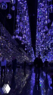 Тёмный зал с множеством подвешенных стеклянных шаров и холодным синим светом, зеркальный пол отражает огоньки и силуэты посетителей.