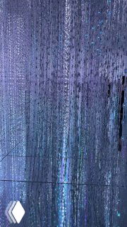 Вертикальные струящиеся световые нити и мерцающие точки, крупный план инсталляции с холодными фиолетово‑синими оттенками и текстурой.