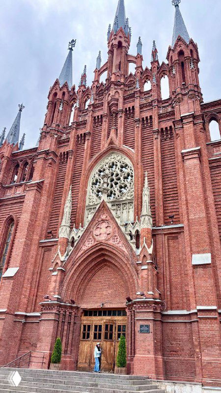 Крупный фрагмент фасада Кафедрального Собора Непорочного Зачатия в Москве: красный кирпич, неоготические шпили и декоративные элементы входной группы.