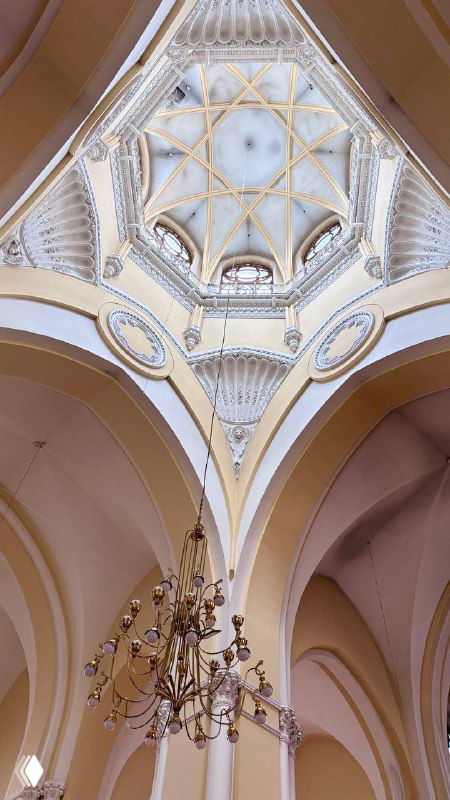 Вид вверх на декоративный купол и перекрытия интерьера собора: позолоченные детали, своды и центральная люстра в нефе католического храма.