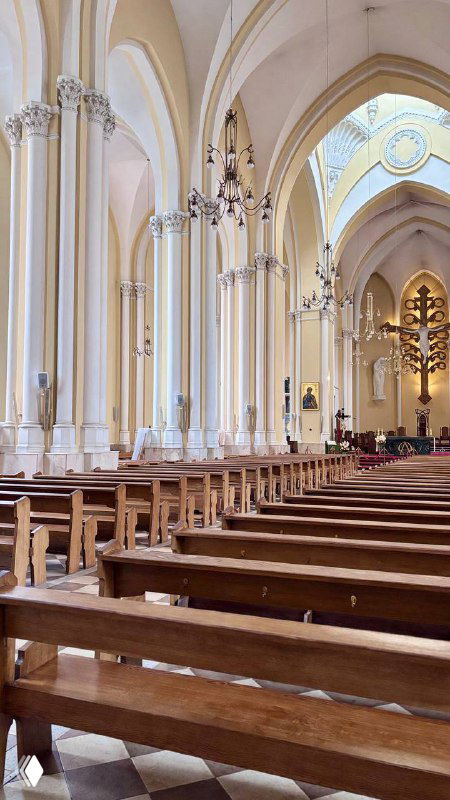 Интерьер корабля собора с рядами деревянных скамеек, центральной осью и алтарной частью, передающими атмосферу литургического пространства.