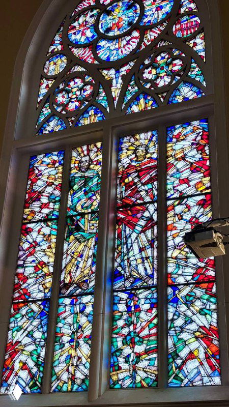 Большой витраж с яркими цветными фрагментами в одном из окон собора: стеклянная композиция добавляет света и художественной детали интерьеру.