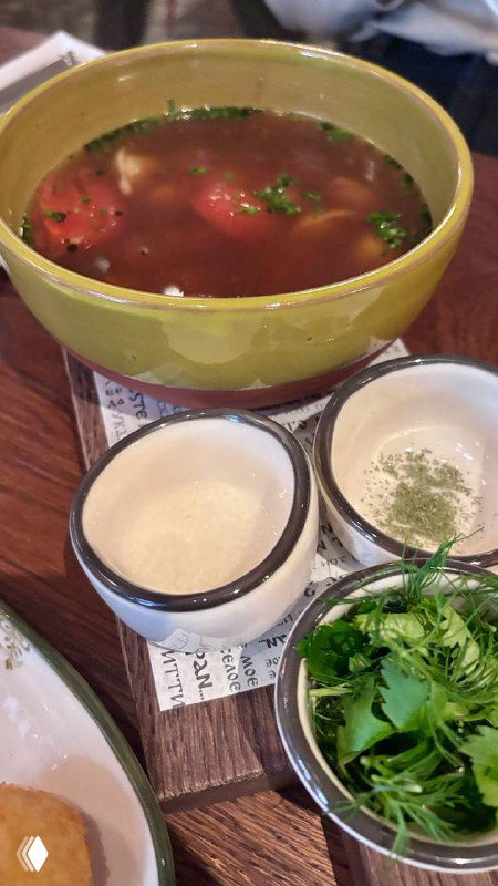 Чаша с азербайджанским супом дюшбара, рядом маленькие пиалы с приправами и зеленью — традиционная подача супа.