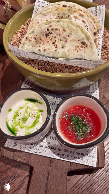 Тарелка с кутабы и несколько соусов в маленьких мисках: творог, зелень и томатный соус — акцент на многообразии вкусов.