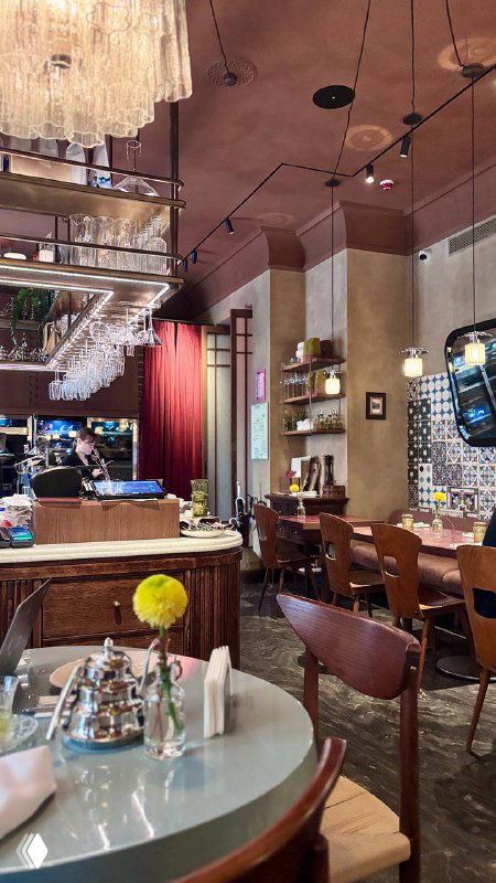 Общий вид зала бистро с барной стойкой, столиками и источниками света — тёплая, гостеприимная обстановка для гурманов.