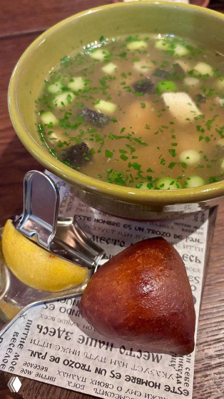 Чаша прозрачного супа с кусочками мяса или рыбы, долька лимона и поданная булочка — подача традиционного первого блюда.