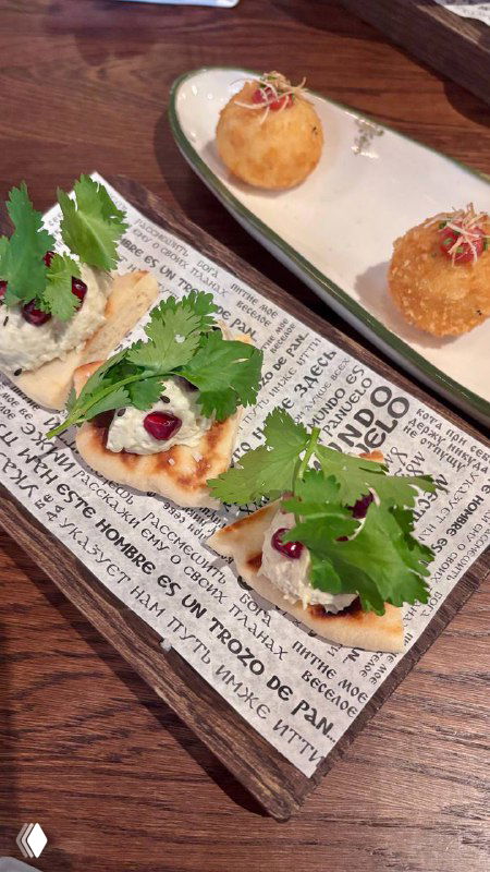 Подача закусок: крокеты с треской и небольшие тосты с зеленью и зернами граната на деревянной доске — декоративная презентация.