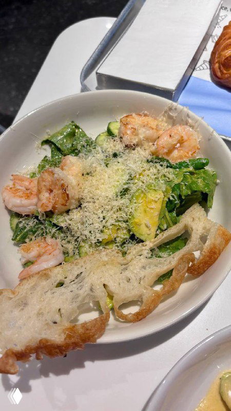 Салат с креветками: листья зелени, креветки, крутоны и тёртый сыр сверху — салат выглядит свежим и аппетитным на светлом столе.