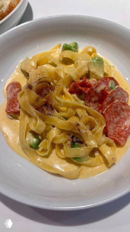 Паста или тёплое блюдо с широкими лентами пасты, кусочками колбасы и кремовым соусом — подача выглядит густой и насыщенной.