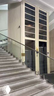 Лестничная площадка внутри Наркомзема с видимыми дверцами и корпусом единственного лифта‑патерностера, перила и мраморные ступени на переднем плане.