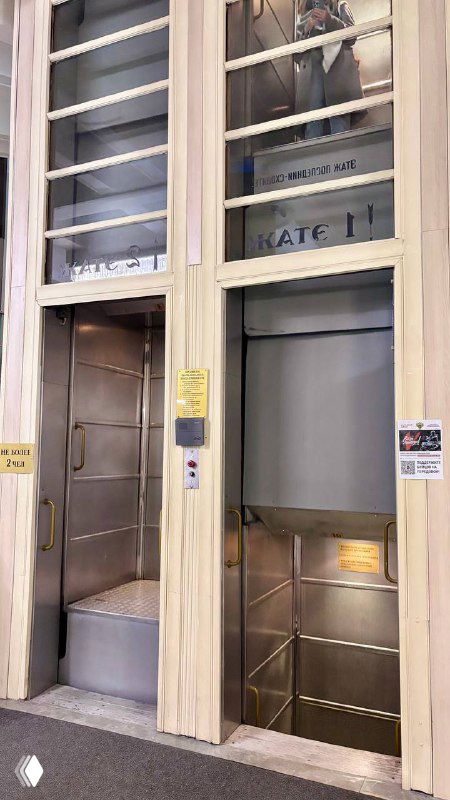 Крупный план внутренней части лифта‑патерностера с открытыми металлическими кабинками и ступенчатой конструкцией, видно механические элементы и створки.