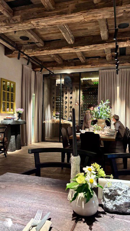 Внутренний интерьер Pomme Verte: деревянные балки на потолке, столы и кресла, цветочные композиции и теплое освещение — атмосфера зала.