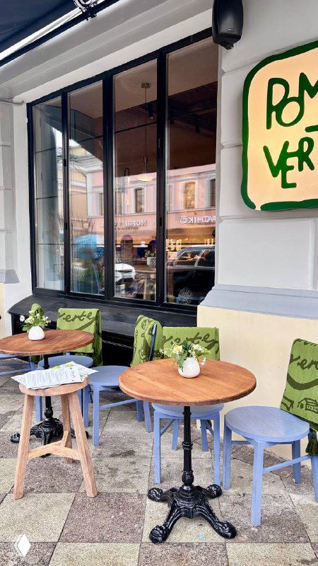 Уличная терраса Pomme Verte: столики у окна, вывеска ресторана и городская улица за стеклом — фасад и уличная посадка заведения.