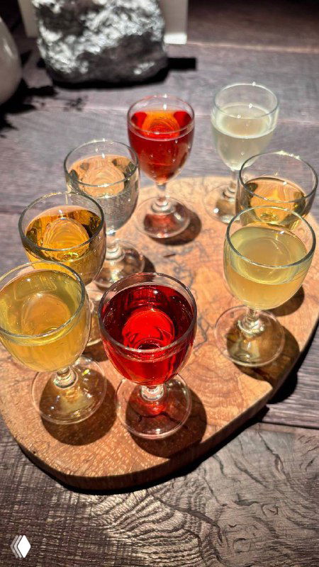 Дегустационный сет сидров: восемь маленьких стопочек разных оттенков напитка на деревянной подставке, вид сверху на столе ресторана.