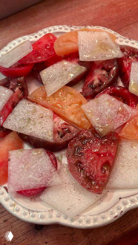 Сезонные разноцветные томаты, поданные со слайсами дыни на фарфоровой тарелке — свежая и нестандартная подача в ресторане.