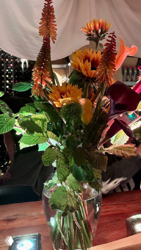 Высокая интерьерная композиция из подсолнухов и декоративных цветов в вазе на столе ресторана — элемент оформления пространства.