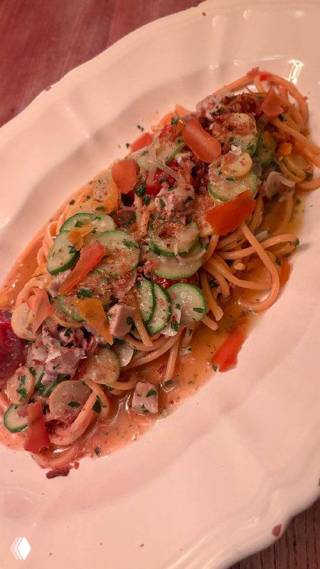 Спагетти с тунцом и овощными лентами в сливочном соусе, подача на длинной белой тарелке — вид сбоку.