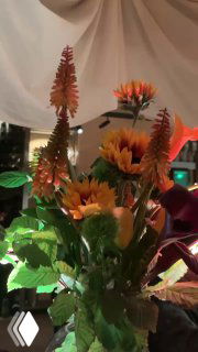 Крупный план букета с высокими оранжевыми цветами и подсолнухами в вазе на столе — декоративный акцент интерьера.