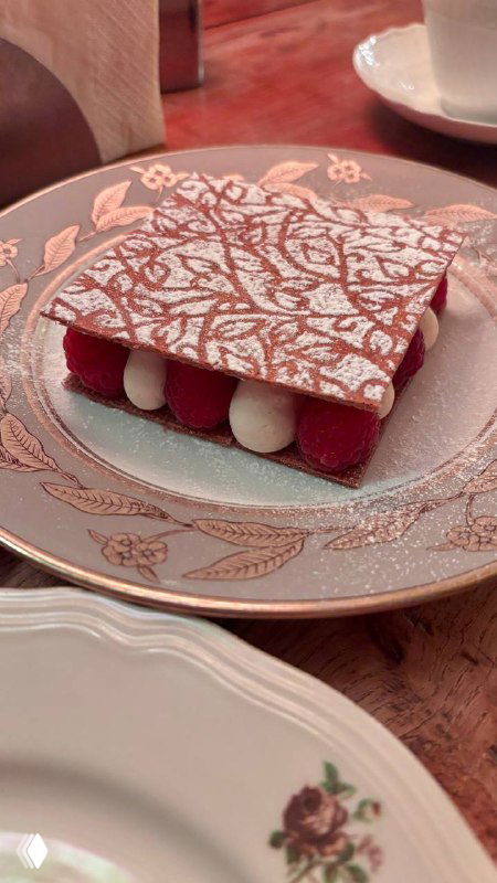 Прямоугольный десерт с яркой красной прослойкой и белыми кремовыми каплями на фарфоровой тарелке — элегантная подача десерта.